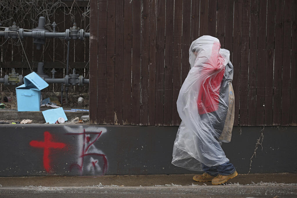 James Andrews uses a plastic bag to stay warm and dry while he walks on Delaware Ave. north of I-244 Wednesday, Feb. 10, 2021 in Tulsa, Okla. (Mike Simons/Tulsa World via AP)