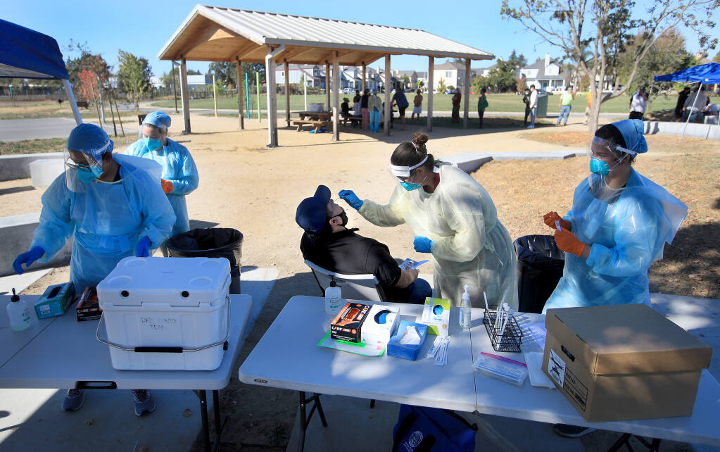 Sergio Guzman of Santa Rosa receives a COVID-19 nose swab from Sonoma County Public Health nurse Devin Andrews as Nicole Callopy assists, Tuesday, Oct. 20, 2020, at Andy's Unity Park in Santa Rosa. At left are Adriana Andres and Ellen Armour. (Kent Porter / The Press Democrat) 2020