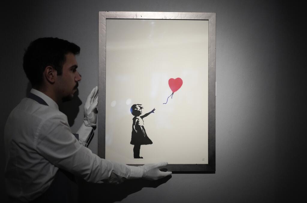 A staff member poses for photographs with a print of "Girl with Balloon, 2004" by British street artist Banksy, at Bonhams auction house in London on Nov. 8, 2021. (AP Photo/Matt Dunham)