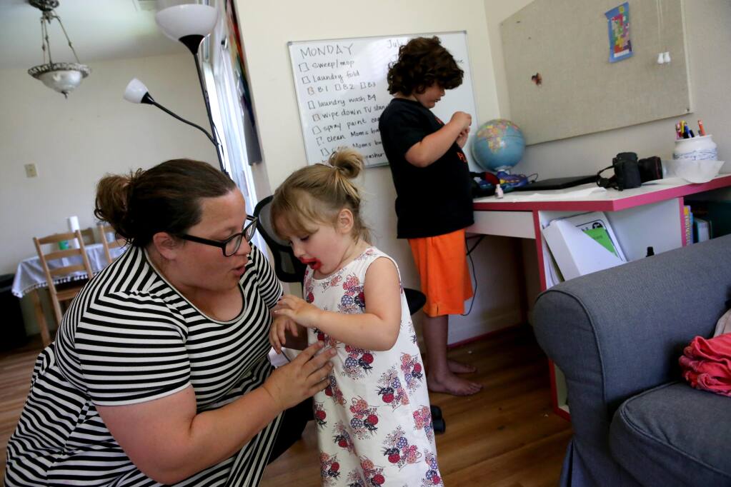 Rachael Hairston Loveridge reacts to the fresh nail polish on the fingertips of her daughter, Helen Loveridge, 2, while her son, Kayden Loveridge, 9, stands at his school desk in their apartment in Sonoma on Monday, July 13, 2020. (Beth Schlanker / The Press Democrat)