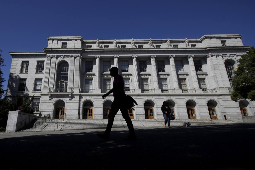 In this March 11, 2020 file photo people walk in front of Wheeler Hall on the University of California campus in Berkeley, Calif. (AP Photo/Jeff Chiu, File)