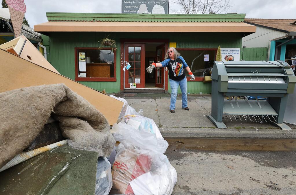 Dee Dee Rydberg throws garbage into her flood damaged materials pile outside of her graphics and printing business in Guerneville on Monday, March 4, 2019. (Christopher Chung/ The Press Democrat)