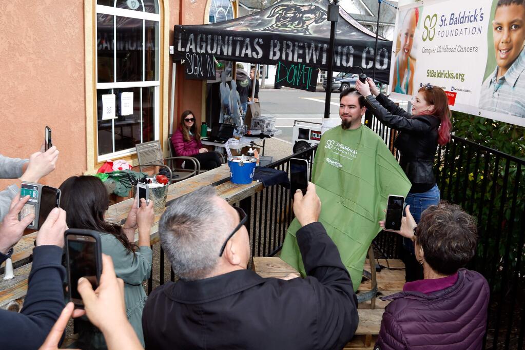 Onlookers snap photos as Carlos Licea, at right, has his head shaved by volunteer barber Nikki Pierce during a fundraiser for the St. Baldrick's childhood cancer research foundation at The Publican in Windsor, California, on Saturday, March 24, 2018. (Alvin Jornada / The Press Democrat)