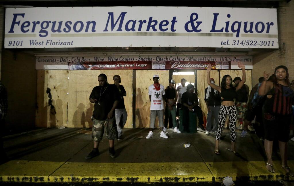 People stand in front of a convenience store after it was looted early Saturday, Aug. 16, 2014, in Ferguson, Mo. The violence stemmed from the shooting death of Michael Brown by police a week ago after the teen allegedly stole a box of cigars from the store. (AP Photo/Charlie Riedel)