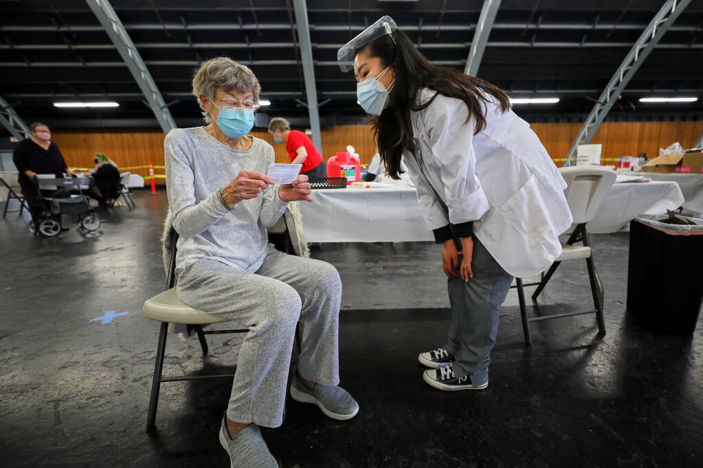 Betsy Todd, left, receives a card for her second coronavirus vaccine appointment after getting her first shot from Safeway pharmacy graduate intern Nancy Kong at a coronavirus vaccination site at the Sonoma County Fairgrounds in Santa Rosa on Wednesday, Feb. 3, 2021. (Christopher Chung / The Press Democrat)