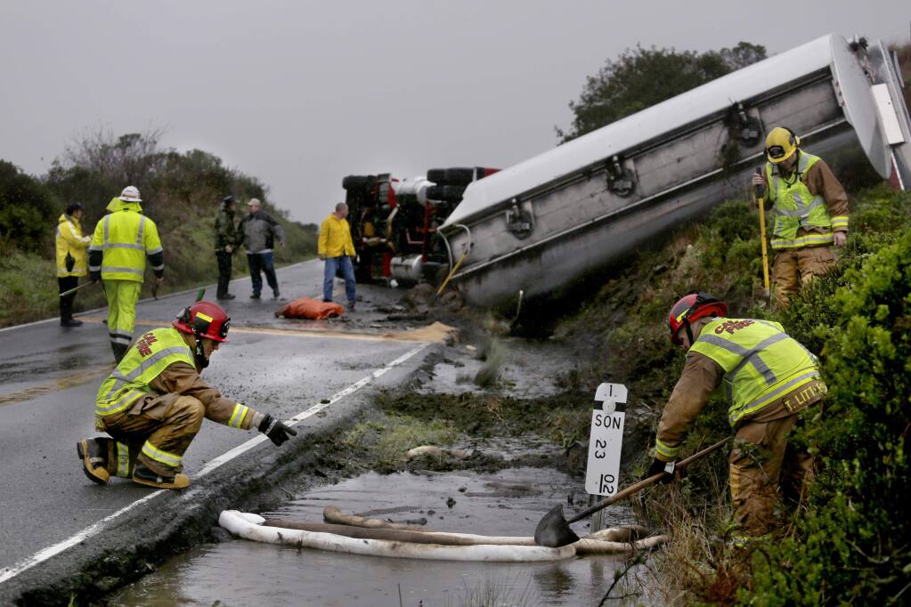 Cal Fire Capt. Paul Mackey, left, and Capt. Trevor Littleton adjust containment booms to corral gasoline after a double-tank fuel truck overturned spilling fuel into a culvert, approximately two miles north of Jenner on Sunday, Feb. 8. (BETH SCHLANKER / The Press Democrat)