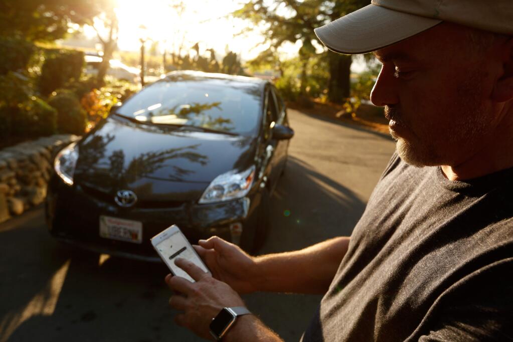 Uber driver Peter Stetson looks as the Uber passenger app in front of his car, in Napa, California on Saturday, November 7, 2015. (Alvin Jornada / The Press Democrat)