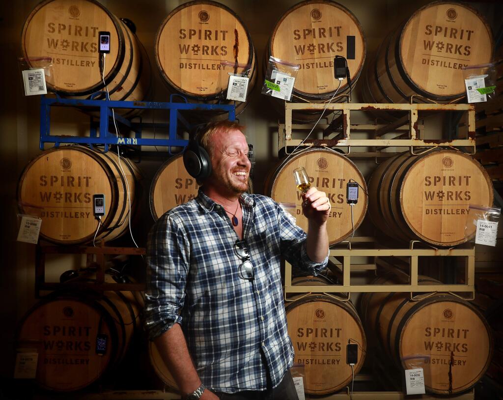 Spirit Works Distillery owner/distiller Timo Marshall samples whiskey that has been listening to Prince and Michael Jackson for three years through headphone attached to the bung. Employees created their own playlists to see whether whiskey tastes better listening to Led Zeppelin or if the control barrels in silence fared better. (John Burgess/The Press Democrat)