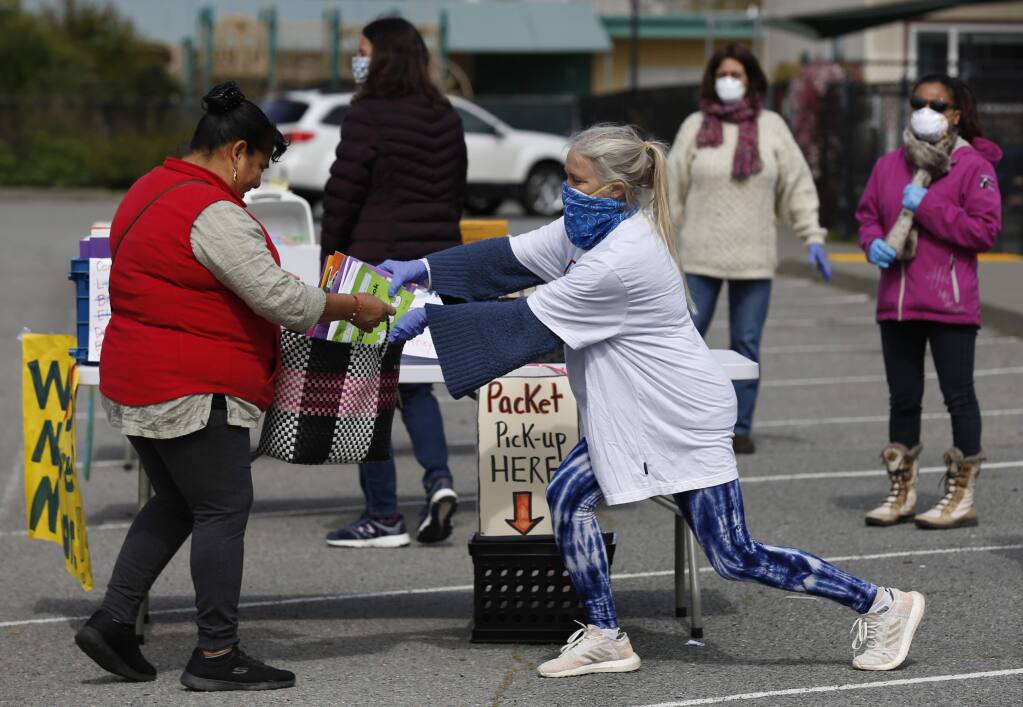 McDowell Elementary School transitional kindergarten teacher Kelly Wood, wearing her husband's bandana over a N95 mask, stretches to put educational material into a bag for a parent outside the school in Petaluma on Monday, April 6, 2020. (BETH SCHLANKER/ The Press Democrat)