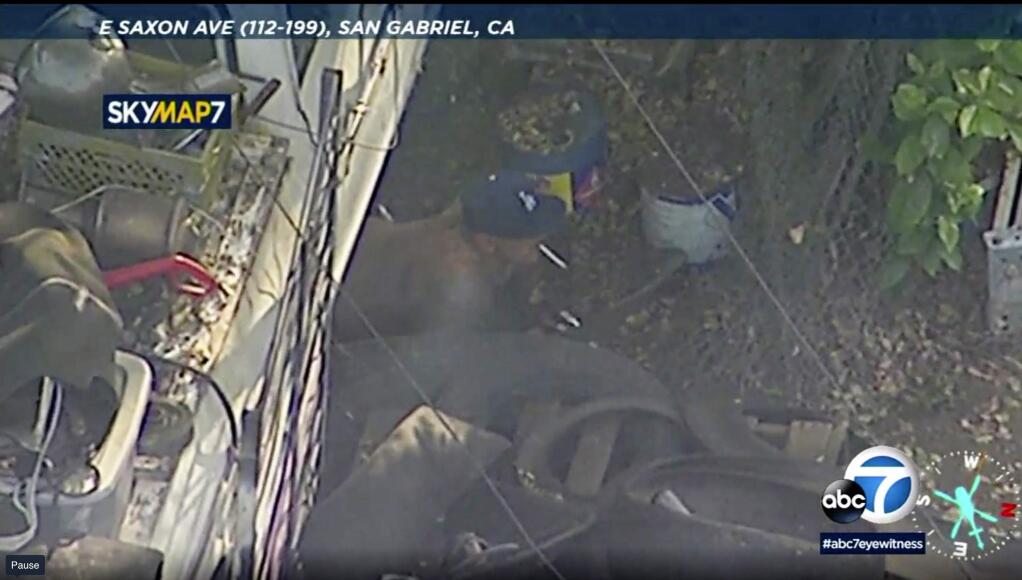 In this photo made from video provided by KABC-TV, a shirtless man crawls out from under a vehicle with a cigarette in his mouth at a property in San Gabriel, Calif. The gunman held police at bay for hours Thursday, set fire to several homes and launched fireworks at surrounding SWAT team members before he charged out of a home with a shotgun and was shot dead, authorities said. (KABC-TV via AP)