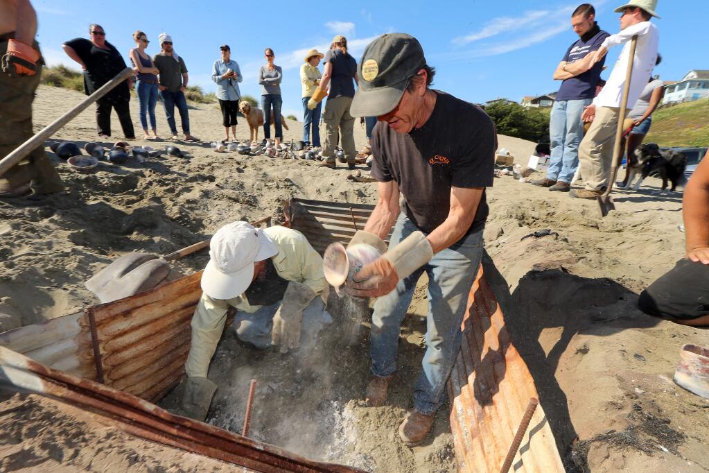 SRJC ceramics instructor Joel Bennett, right, and Barry Southward remove hot ceramics from a fire pit at Dillon Beach after they were fired for 6 hours in sawdust, seaweed and other organic matter. (For the Press Democrat)
