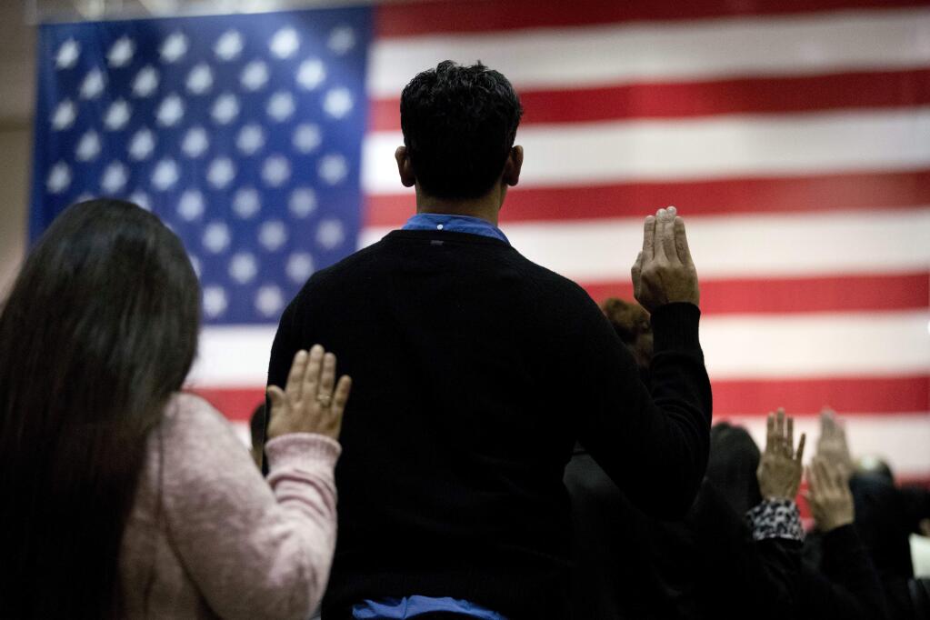 FILE - In this Feb. 15, 2017 file photo, people take the oath of citizenship during a naturalization ceremony at the Los Angeles Convention Center. In a Los Angeles ceremony Wednesday, Sept. 20, 2017, more than 9,000 new American citizens will hear a newly recorded message from President Donald Trump welcoming them to the country and urging them to help others assimilate to help keep the country 'safe, strong and free.' It is the first time the message from Trump will be played at the massive swearing-in ceremonies held each month in Southern California. (AP Photo/Jae C. Hong, File)