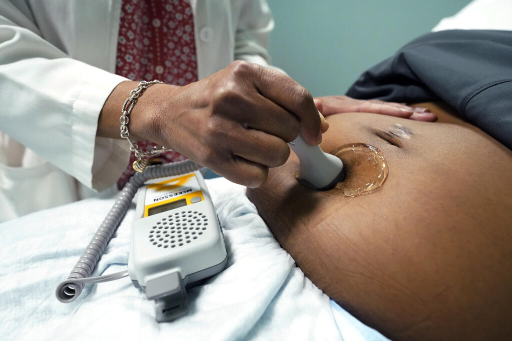FILE - A doctor uses a hand-held Doppler probe on a pregnant woman to measure the heartbeat of the fetus on Dec. 17, 2021, in Jackson, Miss. COVID-19 drove a dramatic increase in the number of women who died from pregnancy or childbirth complications in the U.S. last year, a crisis that has disproportionately claimed Black and Hispanic women as victims, according to a report released Wednesday, Oct. 19, 2022. (AP Photo/Rogelio V. Solis, File)