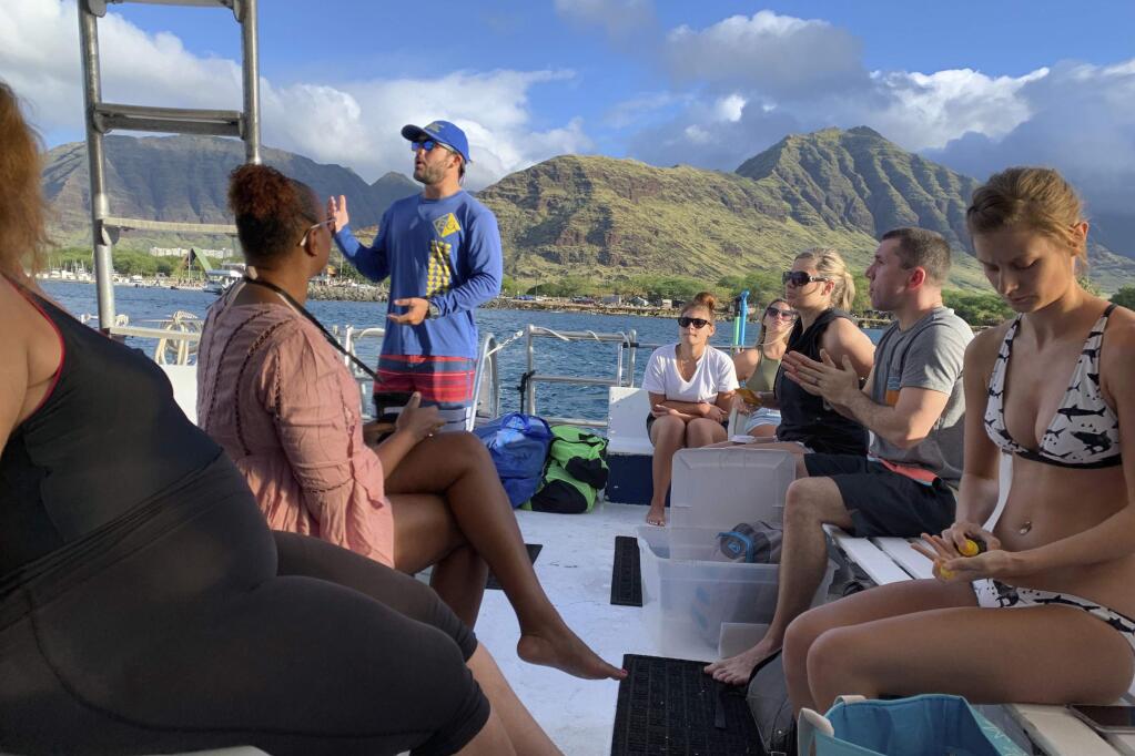 This undated photo provided by EO Waianae Tours shows Bryce Hunter talking to passengers on board a tour boat in Waianae, Hawaii. The coronavirus pandemic has taken out large sections of Hawaii's tourism-based economy, including the EO Waianae Tours dolphin and turtle snorkel tour business run by the Chang family and the family's regular music gig in Waikiki. (Ashlee Jankanish/EO Waianae Tours via AP)