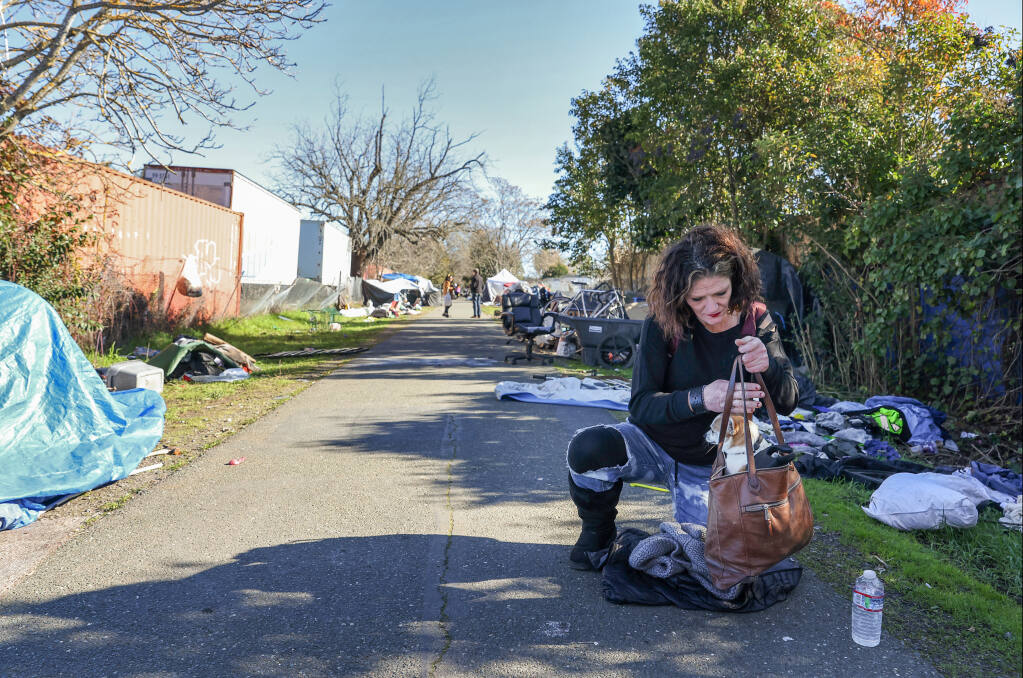 Jen McDonough gathers her dog, Jojo ,into a purse along Joe Rodota Trail, west of Roseland Avenue, in Santa Rosa, Monday, Jan. 23, 2023. McDonough has been living along the trail on and off for three months. (Christopher Chung/The Press Democrat)