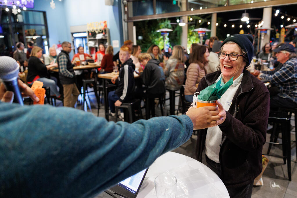 Leslie Mikulich celebrates after winning the raffle during the Redwood Empire Food Bank’s Trivia Night at Barrel Brothers Brewing Kitchen & Cocktails in Windsor, Thursday, Dec. 14, 2023. (Abraham Fuentes / For The Press Democrat)