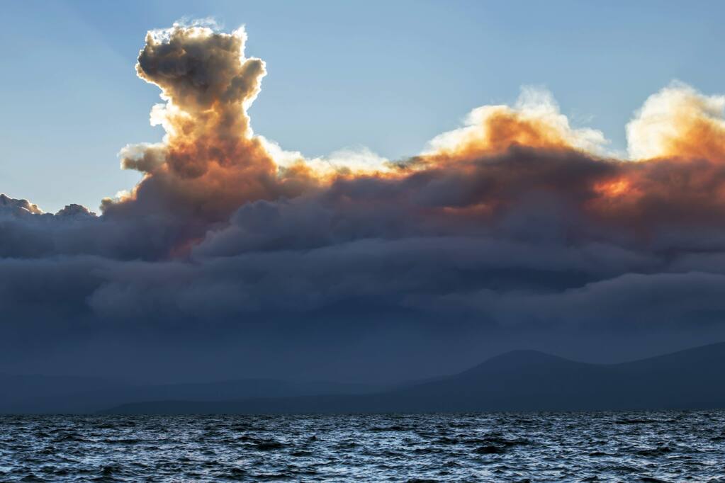 This Wednesday, Sept. 17, 2014 photo shows smoke from a California wildfire rising behind Lake Tahoe as seen from the Nevada side of the lake near Incline Village, Nev. Higher humidity Friday helped slow the growth of the massive Northern California wildfire that authorities say was set deliberately and has forced some 2,800 people to evacuate. (AP Photo/Steve Ellsworth)