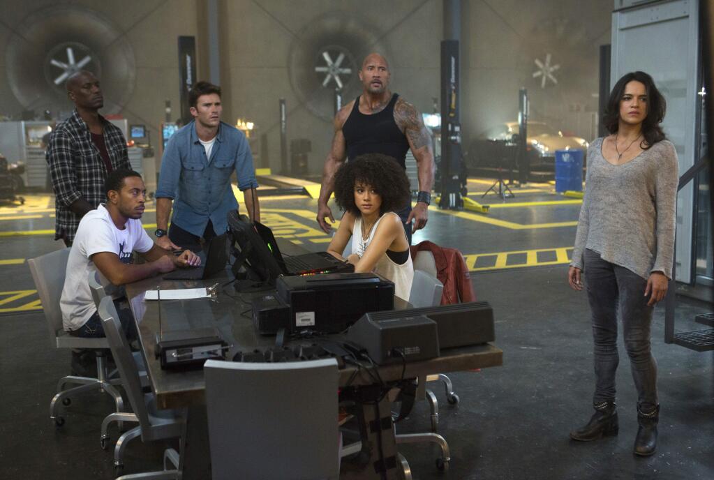 This image released by Universal Pictures shows, Chris 'Ludacris' Bridges, seated left, and Nathalie Emmanuel, seated right, and Tyrese Gibson, standing from left, Scott Eastwood, Dwayne Johnson and Michelle Rodriguez in 'The Fate of the Furious.' (Matt Kennedy/Universal Pictures via AP)