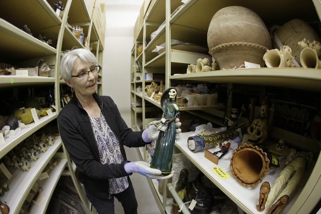 In this photo taken Monday, June 27, 2016, registrar Wendy Niles holds a Day of the Dead sculpture 'La Soldadera' by Alvaro de la Cruz being stored in a vault at the Mexican Museum currently located at Fort Mason in San Francisco. Construction of a four-story, state-of-the-art Mexican Museum is underway, realizing the dream of a late Mexican-American artist who four decades ago opened the city's first museum for Latino art in a Mission District storefront. The 60-000 square feet building in downtown San Francisco will be home to 16,000 pre-Columbian, colonial, modern and contemporary works of Mexican, Mexican-American and Latino art, the largest such collection in the country. (AP Photo/Eric Risberg)