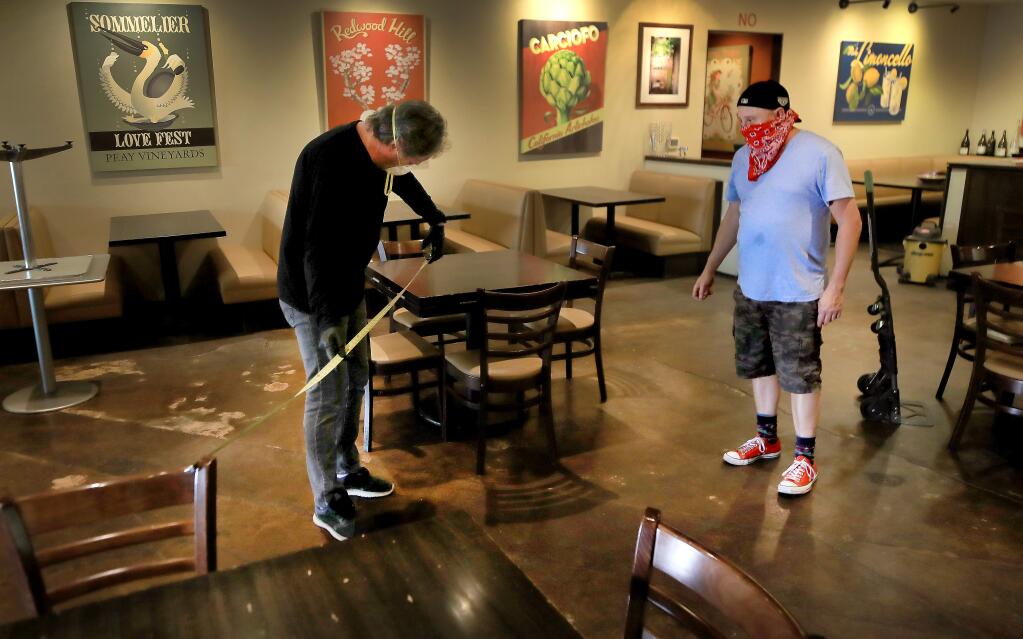 Rosso Pizzeria owner Kevin Cronin, left, and general manager Richie Hovden use a tape measure to distance out tables, Tuesday, May 12, 2020 in response to an announcement that restaurants can open up with social distancing and other precautions in the coming days. They are also planning to install plexiglas between the booths. (Kent Porter / The Press Democrat) 2020
