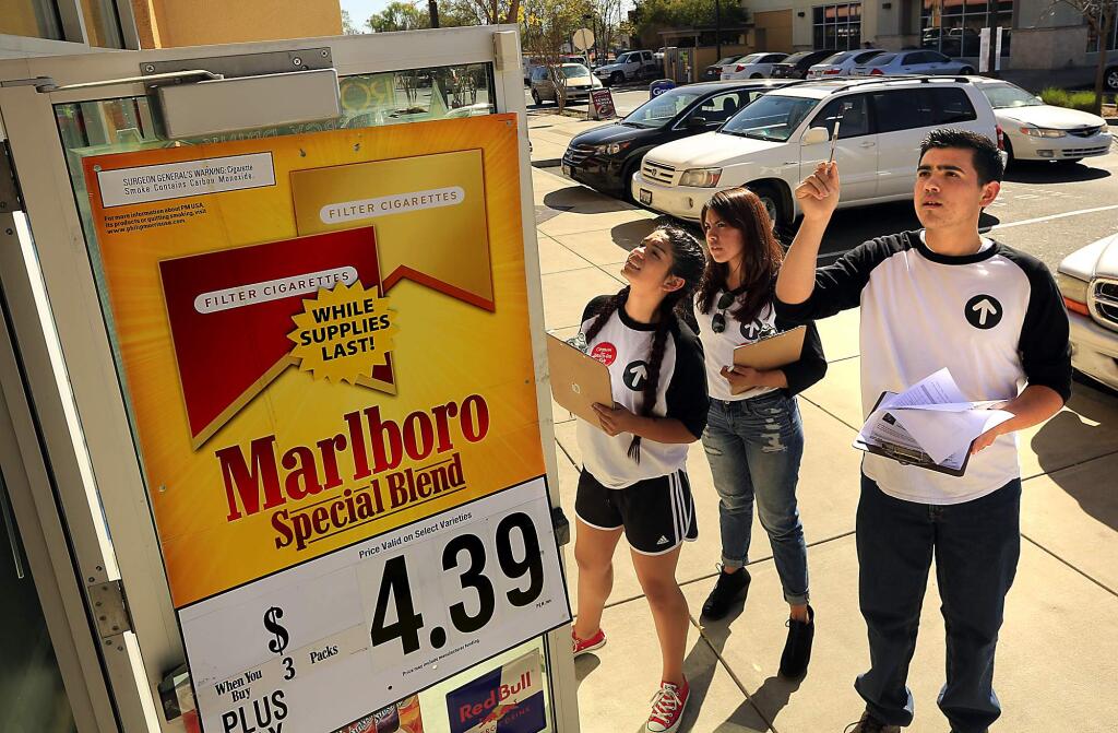 Roseland University Prep students Paola Auilar, 17, left, Carla Rodriguez, 16, and Miguel Garduno, 16, count the tobacco, e-cigarette and alcohol ads on the outside of Stony Point Wine and Liquor Store during a survey of stores within a mile of their high school. (Photo by John Burgess/The Press Democrat)