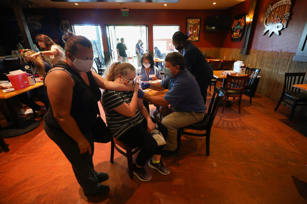 Dr. John Tomasin, right, administers a dose of the Pfizer COVID-19 vaccine to Kadin Anderson, 13, as she holds her mother Shannon's hand for support, during a Sonoma County Medical Association vaccination clinic at Bear Republic Brewing Company in Rohnert Park on Thursday, May 27, 2021.  (Christopher Chung/ The Press Democrat)