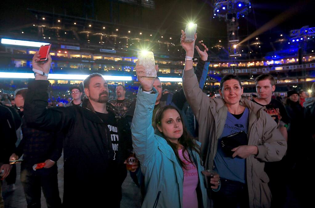 Tim and Lori Sarver, left, and Justin and Hollie Tracy lost their homes in Coffey Park in the Tubbs fire, acknowledging their loss by using their phones during Band Together benefit concert for North Bay fire relief in San Francisco, Thursday Nov. 9, 2017. (Kent Porter / The Press Democrat)