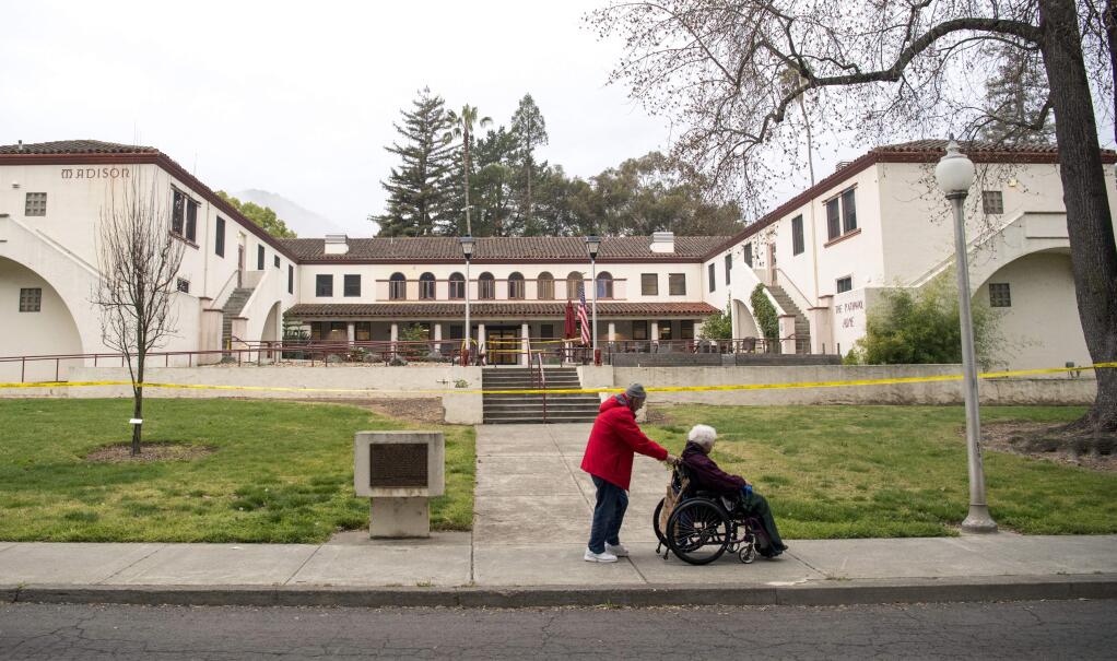 A man pushes a woman in a wheelchair past the Veterans Home of California, the morning after a hostage situation in Yountville, Calif., on Saturday, March 10, 2018. A daylong siege at The Pathway Home ended Friday evening with the discovery of four bodies, including the gunman, identified as Albert Wong, a former Army rifleman who served a year in Afghanistan in 2011-2012. (AP Photo/Josh Edelson)