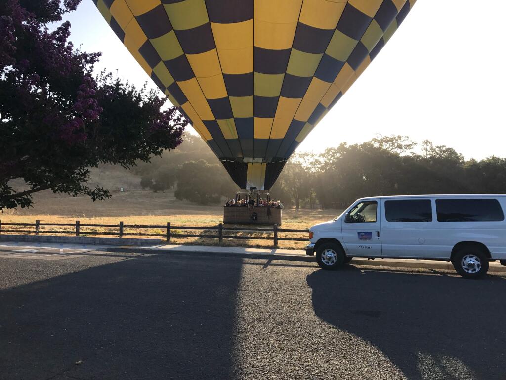 A hot-air balloon with about 20 people in its gondola touches down in the field near Montini Preserve, near the Vallejo House at Sonoma State Historic Park. A van from Balloons Above Napa Valley is parked nearby. (Caitlin Cornwall)