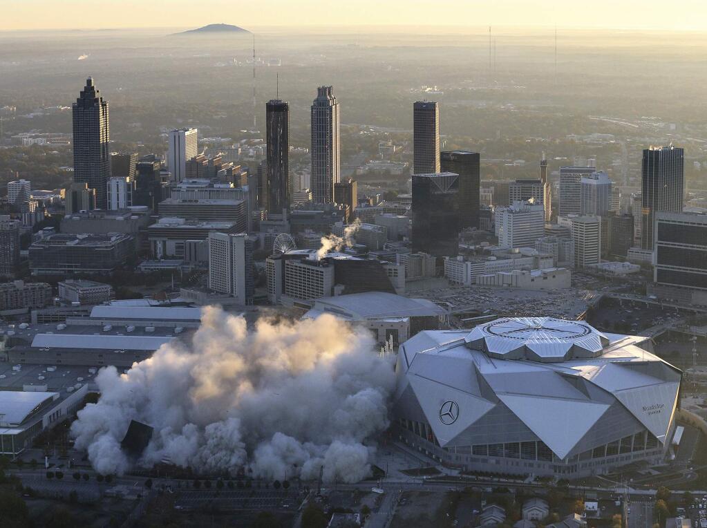 The Georgia Dome is destroyed in a scheduled implosion next to its replacement the Mercedes-Benz Stadium, right, Monday, Nov. 20, 2017, in Atlanta. The dome was not only the former home of the Atlanta Falcons but also the site of two Super Bowls, 1996 Olympics Games events and NCAA basketball tournaments among other major events. (Curtis Compton/Atlanta Journal-Constitution via AP)