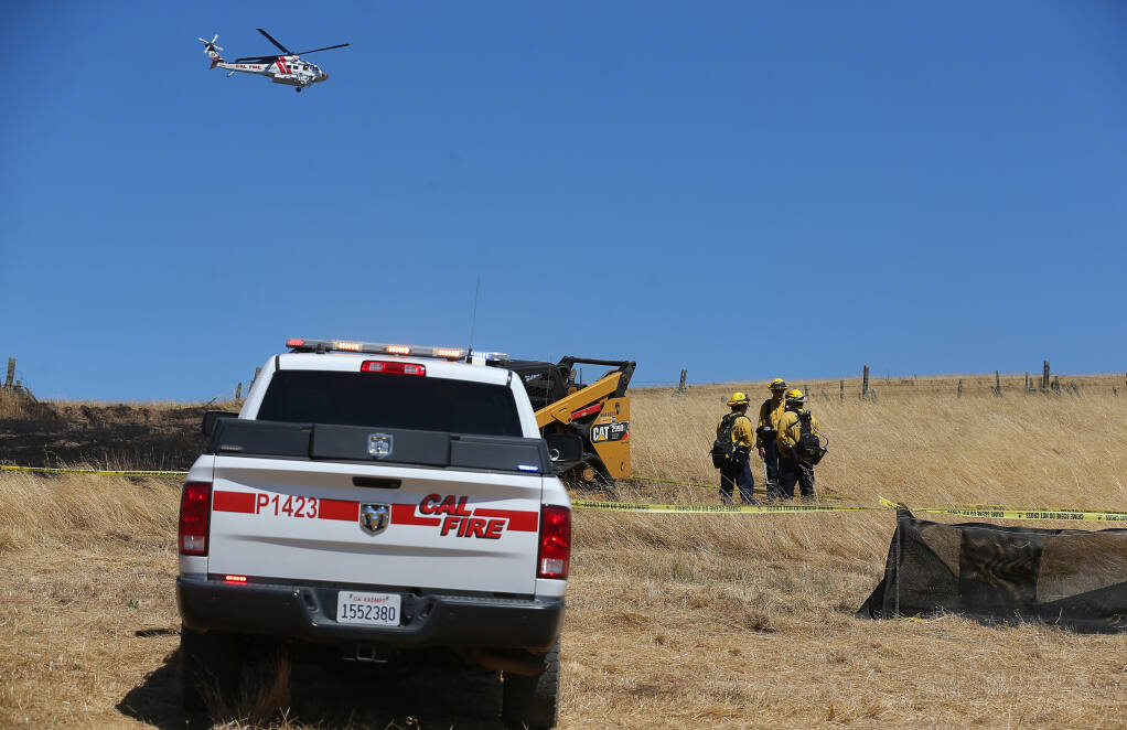 Cal Fire personnel stand near a compact track loader where an individual died in the Roblar Fire near Hessel on Monday, June 27, 2022.  (Christopher Chung/The Press Democrat)