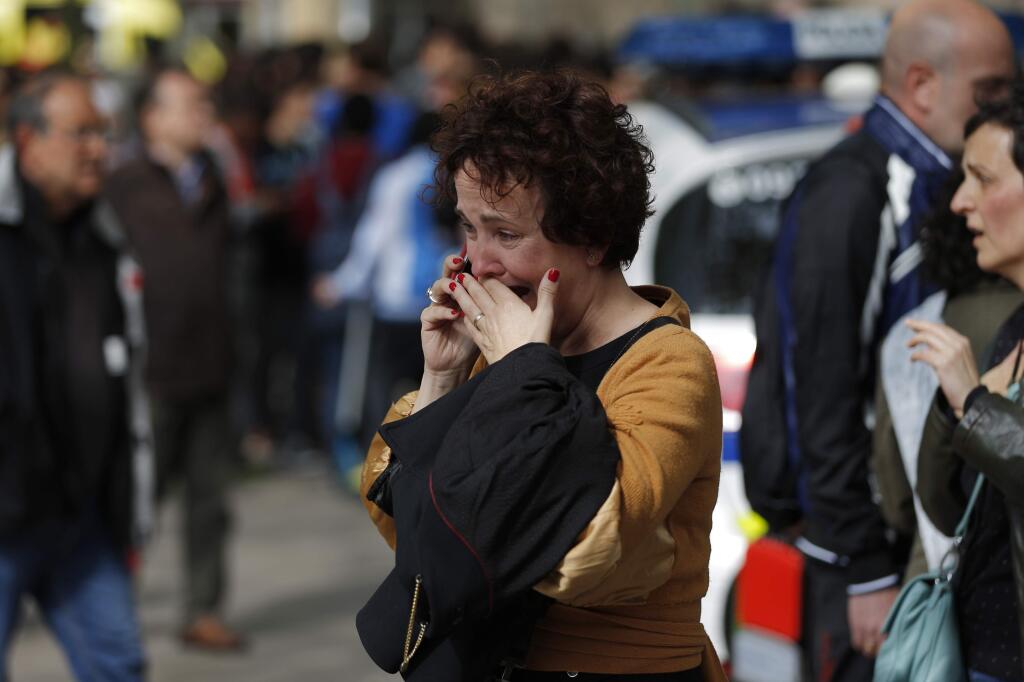 A woman speaks on a cell phone outside the high school in Barcelona, Spain, Monday, April 20, 2015, where a minor has been taken into custody. Police in the northeastern city of Barcelona have detained a youth suspected of having a killed a teacher and wounded several other people inside a school. A regional police spokesman said the minor was detained Monday. The officer was not immediately able to confirm what weapon was used to kill the male teacher but Spanish National Television and other media outlets said it was a crossbow. (AP Photo/Emilio Morenatti)