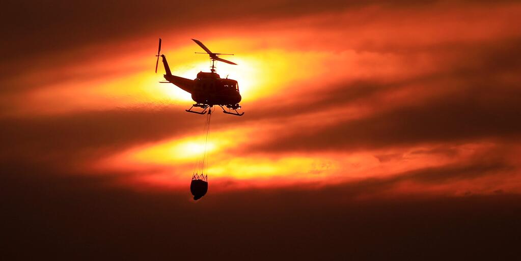 The setting sun is tinged by wildfire smoke and cirrus clouds as the Boggs Mountain Cal Fire Helitack pilot steers the Bell UH-1H Huey helicopter to make a drop in the 500-acre American Fire in Napa/Solano County on Sunday, Oct. 5, 2019 in American Canyon. (Kent Porter / The Press Democrat)