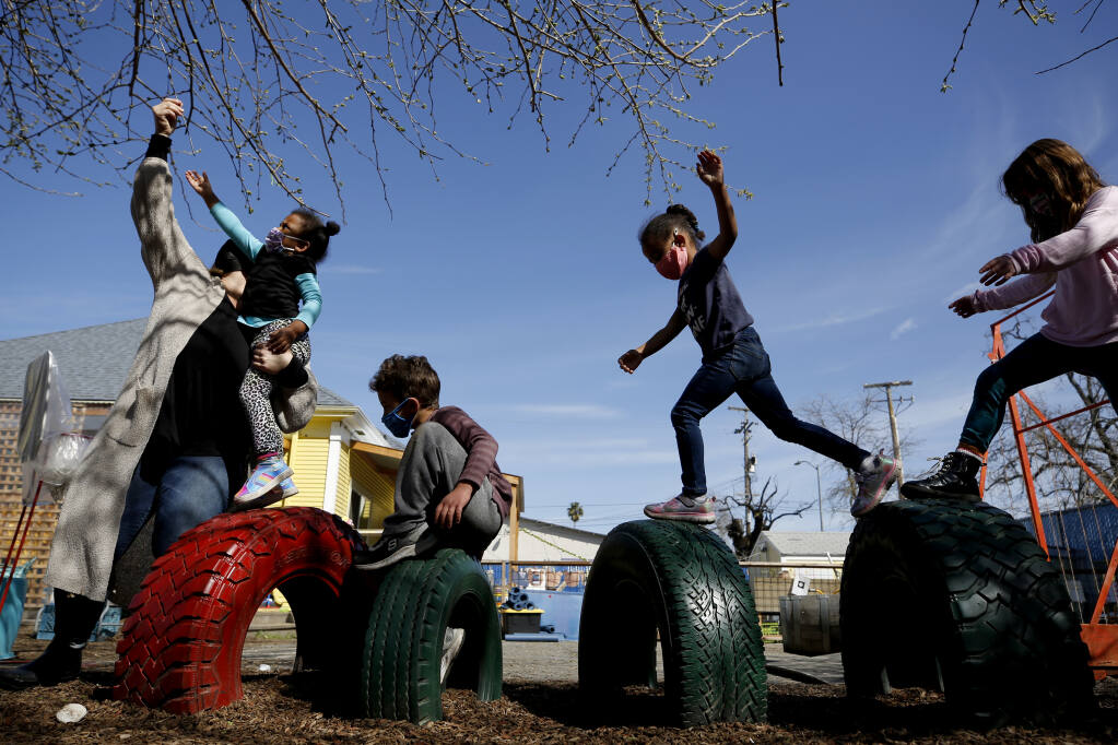 Teacher Amelia Ziraldo, left, reaches to pull down a tree branch for her students to swing from at Storybook Village Preschool in Santa Rosa, Calif., on Tuesday, March 16, 2021. (Beth Schlanker/ The Press Democrat)