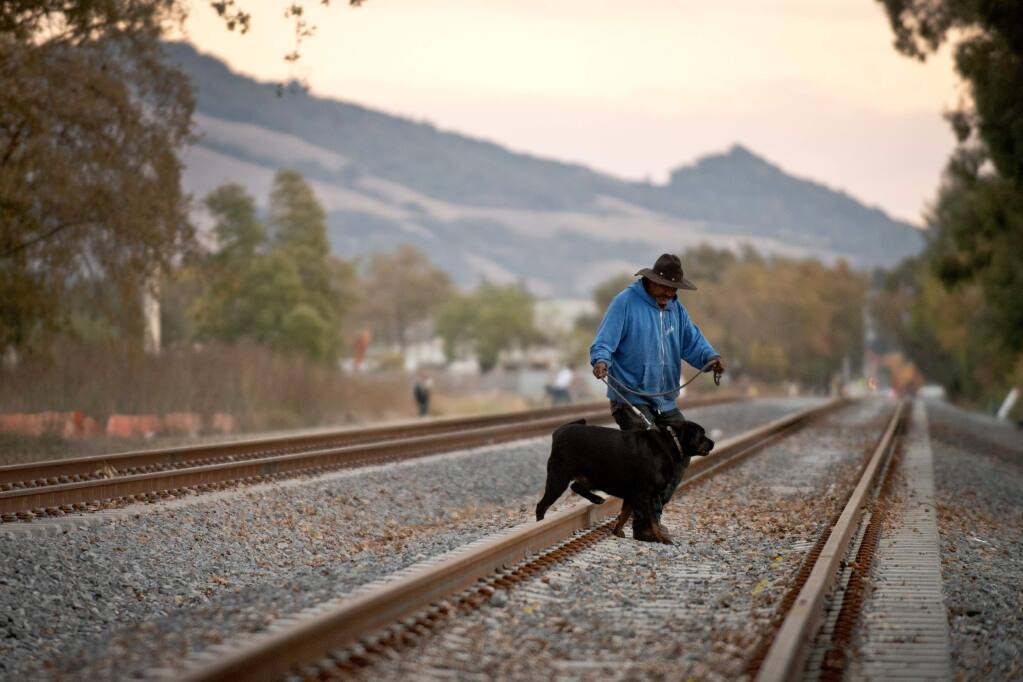 Jorge Robles walks his dog, Gordo, across railroad tracks that split Jennings Avenue near North Dutton Avenue in Santa Rosa in 2013. (ALVIN JORANDA/ PD FILE)