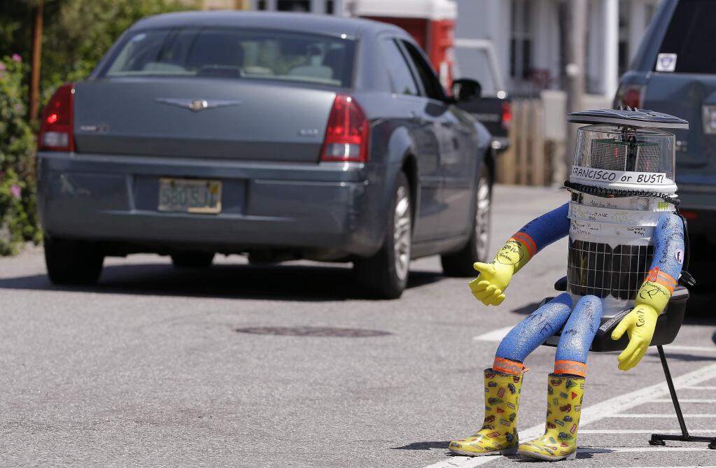 FILE- In this July 17, 2015, file photo, a car drives by HitchBOT, a hitchhiking robot in Marblehead, Mass. The Canadian researchers who created hitchBOT as a social experiment say someone in Philadelphia damaged the robot beyond repair on Saturday, Aug. 1, ending its brief American tour. The robot was trying to travel cross-country after successfully hitchhiking across Canada last year and parts of Europe. (AP Photo/Stephan Savoia, File)