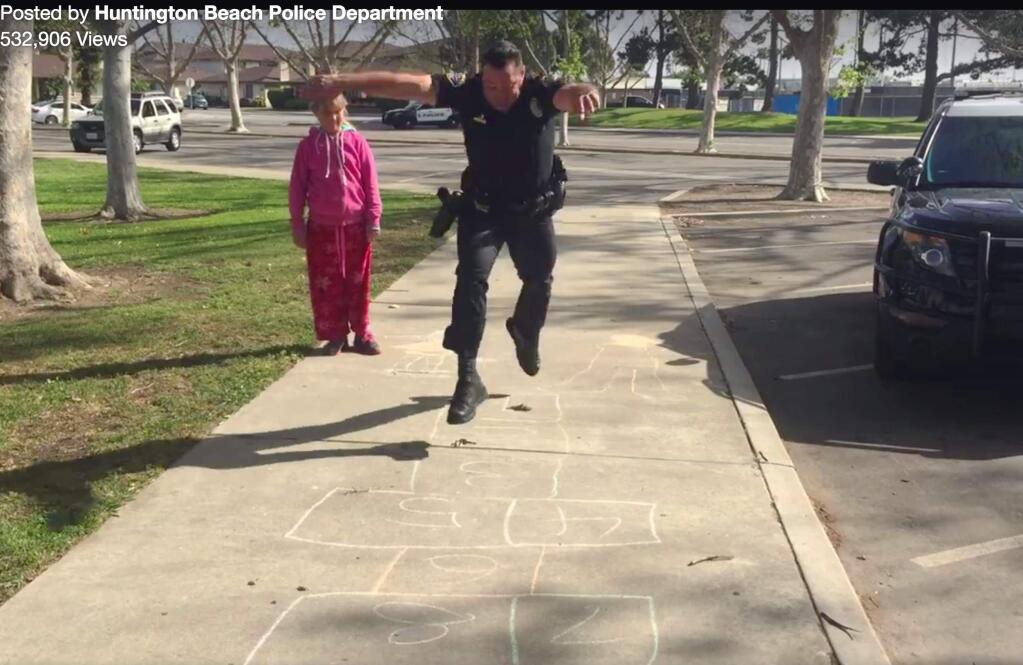 In this Wednesday, March 30, 2016 still frame from video provided by the Huntington Beach, Calif., Police Department, Officer Zach Pricer shows an 11-year-old homeless girl how to hopscotch on a street in Huntington Beach, Calif. Officers found the girl and her mother living in a car in a parking lot Wednesday. While other officers reached out to the department's homeless task force, Pricer turned to hopscotch to make the girl feel more comfortable, knowing a police officer can seem scary to a child. (Huntington Beach Police Department via AP)