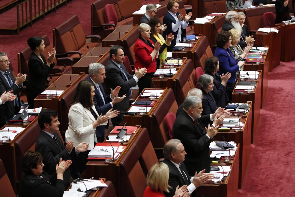 Members of the Senate stand and applaud Attorney-General George Brandis who chastised an Australian senator who provoked an angry backlash from lawmakers by wearing a burqa in Parliament House in Canberra, Australia, Thursday, Aug. 17, 2017. Pauline Hanson, leader of the anti-Muslim, anti-immigration One Nation minor party, sat wearing the black head-to-ankle garment for more than 10 minutes before taking it off as she rose to explain that she wanted such outfits banned on national security grounds.(Jed Cooper/Australian Broadcasting Corp. via AP)