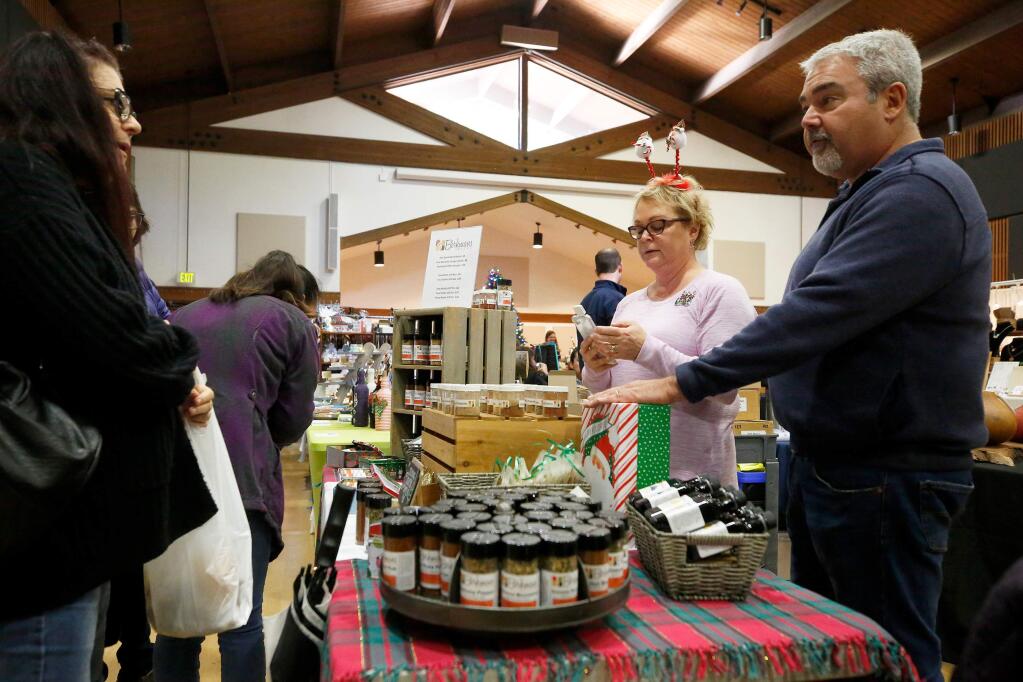 Phil and Heidi Schneider, right, owners of Berkmans Spices talk with customer Jacquie Lamica of Santa Rosa, who has ordered products online from Berkmans Spices, but made a purchase at their display table during the Holiday Arts and Crafts Faire at the Rohnert Park Community Center, in Rohnert Park, California, on Friday, November 29, 2019. (Alvin Jornada / The Press Democrat)