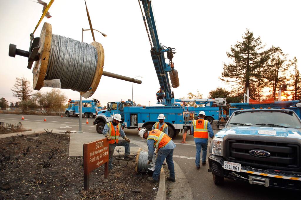 PG&E crews hoist spools of guy wire needed to provide backup tension for the power line they were about to string across Highway 101 to restore power to parts of north Santa Rosa, Oct. 11, 2017. (Alvin Jornada / The Press Democrat)