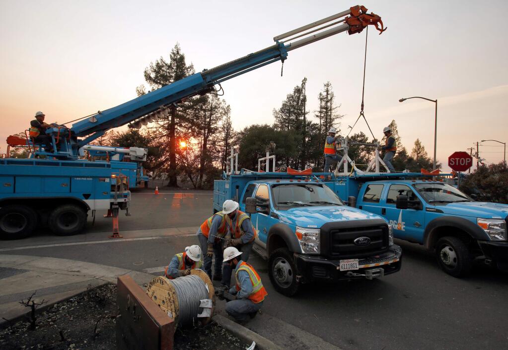 PG&E crews hoist spools carrying 2,500-feet of guy wire to provide backup tension for a power line they are stringing across Highway 101 to restore power in parts of north Santa Rosa, California on Wednesday, Oct. 11, 2017. (Alvin Jornada / The Press Democrat)