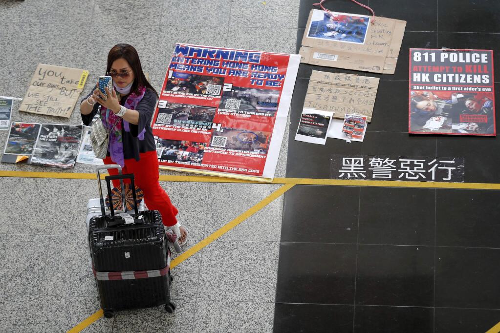 A traveller takes a smartphone photo near placards and posters placed by protesters at the airport in Hong Kong, Wednesday, Aug. 14, 2019. Flight operations resumed at the airport Wednesday morning after two days of disruptions marked by outbursts of violence highlighting the hardening positions of pro-democracy protesters and the authorities in the Chinese city that's a major international travel hub. (AP Photo/Vincent Thian)