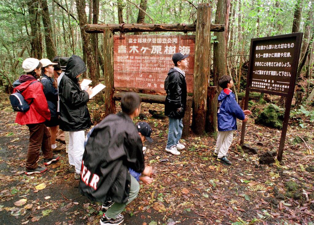 FILE - in this Thursday, Oct. 22, 1998, file photo a group of schoolchildren read signs posted in the dense woods of the Aokigahara Forest at the base of Mount Fuji, Japan. American blogger Logan Paul is apologizing after getting slammed for a video he shared on YouTube that appeared to show a dead body in the Aokigahara Forest in Japan, which is famous as a suicide spot. The sign at right reads: 'Your life is a precious gift from your parents. Once again, try to remember your parents, brothers and sisters and think about your children.' (AP Photo/Atsushi Tsukada, File)