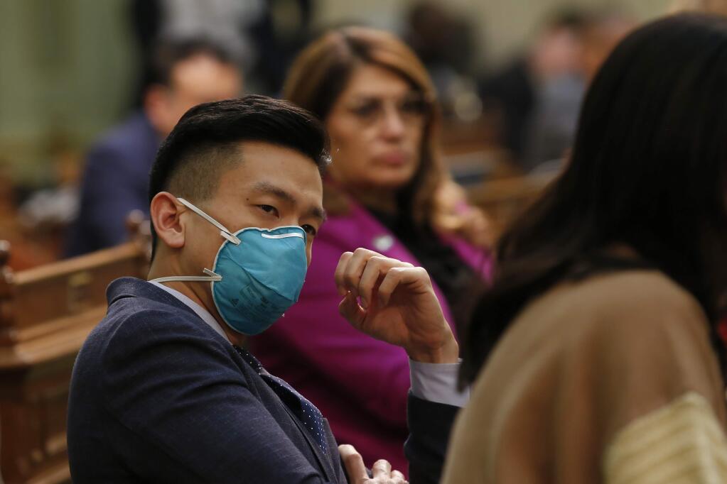 Assemblyman Evan Low, D-San Jose, wears a mask as listens to lawmakers discuss a pair of bills dealing with the coronavirus at the Capitol in Sacramento, Calif., Monday, March 16, 2020. Low, whose district encompasses Santa Clara County that has had 79 confirmed cases of the coronavirus, wore the mask as precaution. (AP Photo/Rich Pedroncelli)