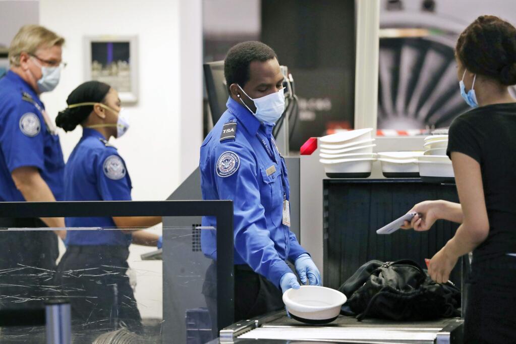 FILE - In this May 18, 2020 file photo TSA officers wear protective masks at a security screening area at Seattle-Tacoma International Airport in SeaTac, Wash. A high-ranking Transportation Security Administration official says the agency is falling short when it comes to protecting airport screeners and the public from the new coronavirus, according to published reports. A federal office that handles whistleblower complaints has ordered an investigation. (AP Photo/Elaine Thompson, File)