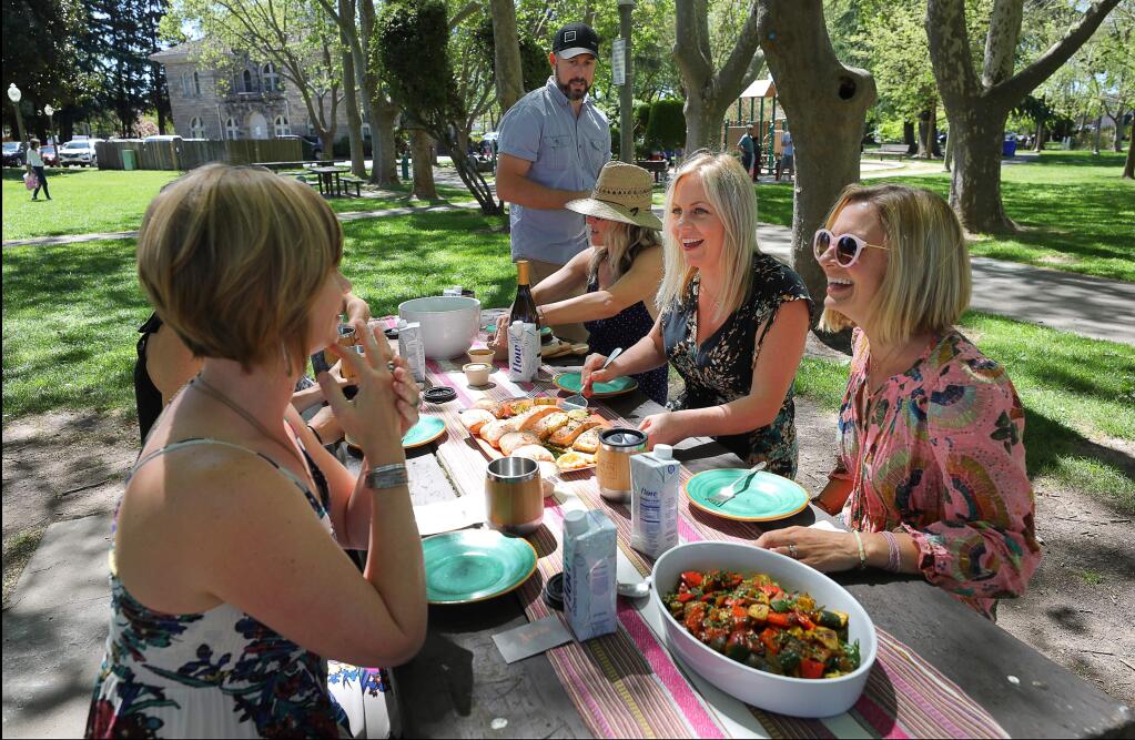 Allyson Weekes, second from right, and her husband Nigel Weekes, standing, serve lunch to friends Jacqui Kotula, right, Lisa Hanson, and Angela Martin in Sonoma Plaza, after taking them wine tasting at Three Sticks Wines on Monday, April 22, 2019. Allyson and Nigel Weekes own Bohemian Highway Tourism Company.(Christopher Chung/ The Press Democrat)