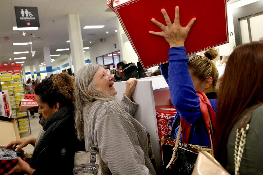 Shopper Patty Culmore, left, watches as Esmeralda Navarro raises multiple boxes of boots over her head at JCPenny in Santa Rosa on Thursday, November 22, 2018. (BETH SCHLANKER/ The Press Democrat)
