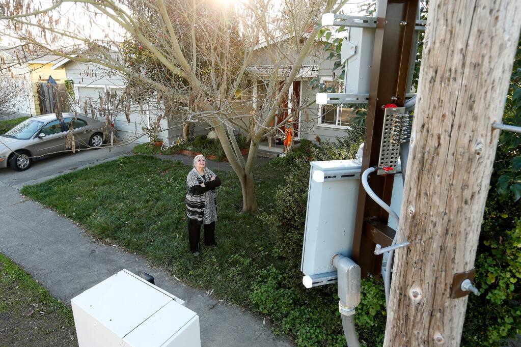 Judith Monroy poses for a portrait in her front yard, looking up at a Verizon Wireless cell signal booster, on a utility pole at right, and its in-ground utility box, lower left, that were installed in front of her home on Link Lane in Santa Rosa, California, on Friday, January 12, 2018. Neighborhood residents are upset at Verizon Wireless because only one resident, Monroy's next door neighbor, was notified in writing prior to the installation, as well as the size and proximity of the transmitters to their homes. (Alvin Jornada / The Press Democrat)