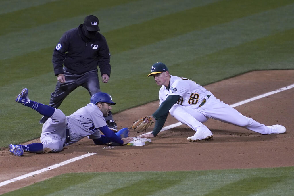 Los Angeles Dodgers' Chris Taylor, bottom left, slides safely into third base next to Oakland Athletics third baseman Matt Chapman during the third inning of a baseball game in Oakland, Calif., Monday, April 5, 2021. Umpire Sean Barber, top left, looks on. (AP Photo/Jeff Chiu)