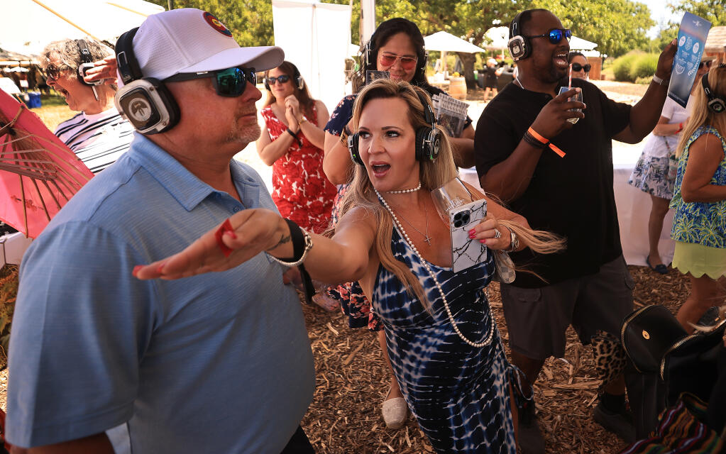 Tamy Akers modifies her dance moves in from of husband Lucas as part of a silent disco during the Taste of Sonoma, Saturday, June 25, 2022 held at the Kendall-Jackson Wine Estate & Gardens near Santa Rosa. In the background are Arlene, middle left, and husband Vohn White        (Kent Porter / The Press Democrat) 2022